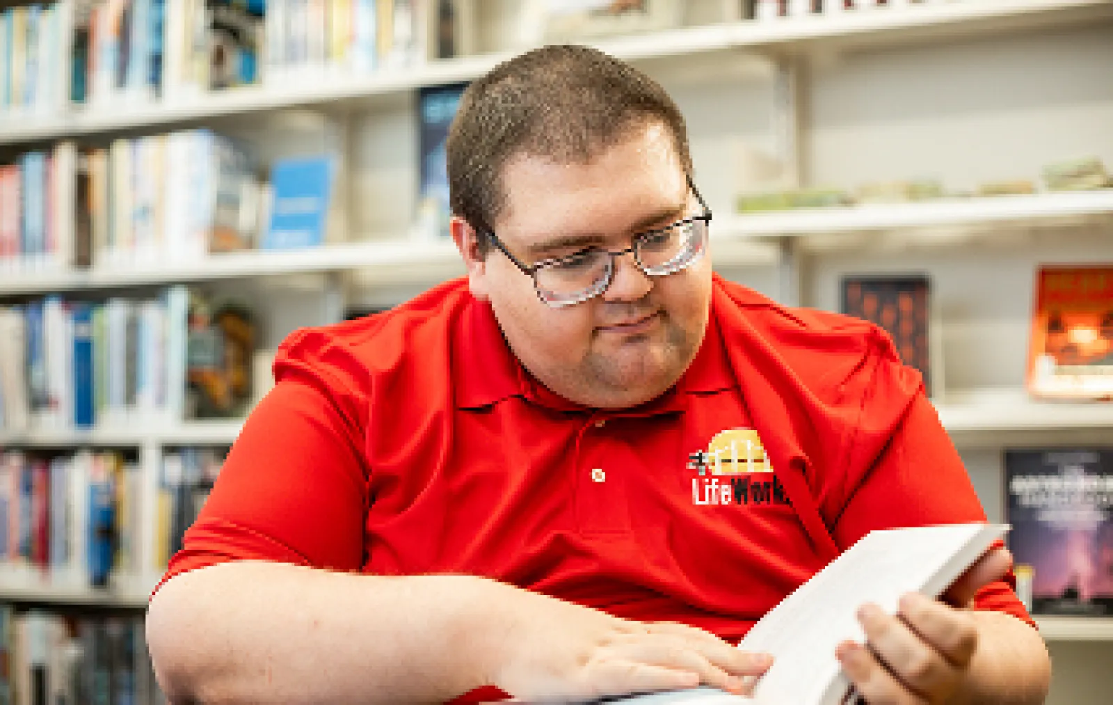 LifeWorks participant in a red branded polo reading a book in the library