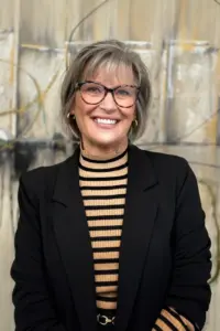 Joanie O'Bryan Headshot smiling in front of yellow and grey painting