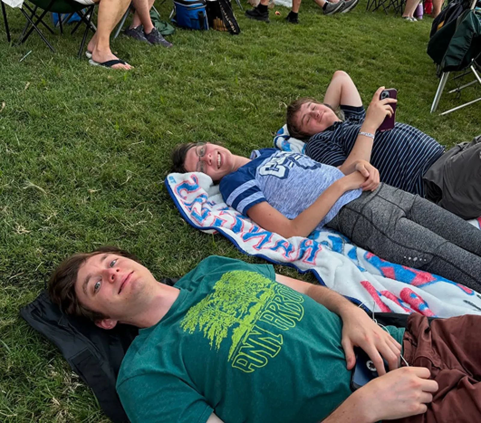Three male LifeWorks participants are laying on blankets in the grass smiling at the camera during a group activity.