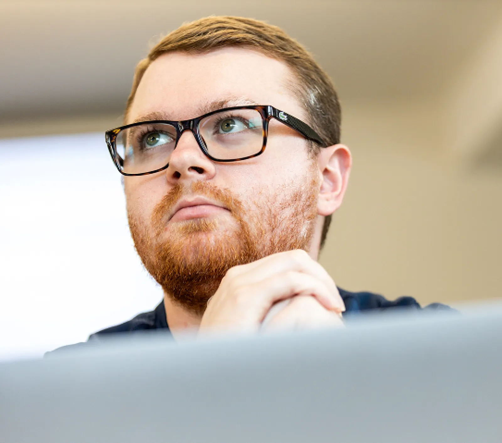 A young male with glasses is looking off camera listening to an instructor with is hands clasped.