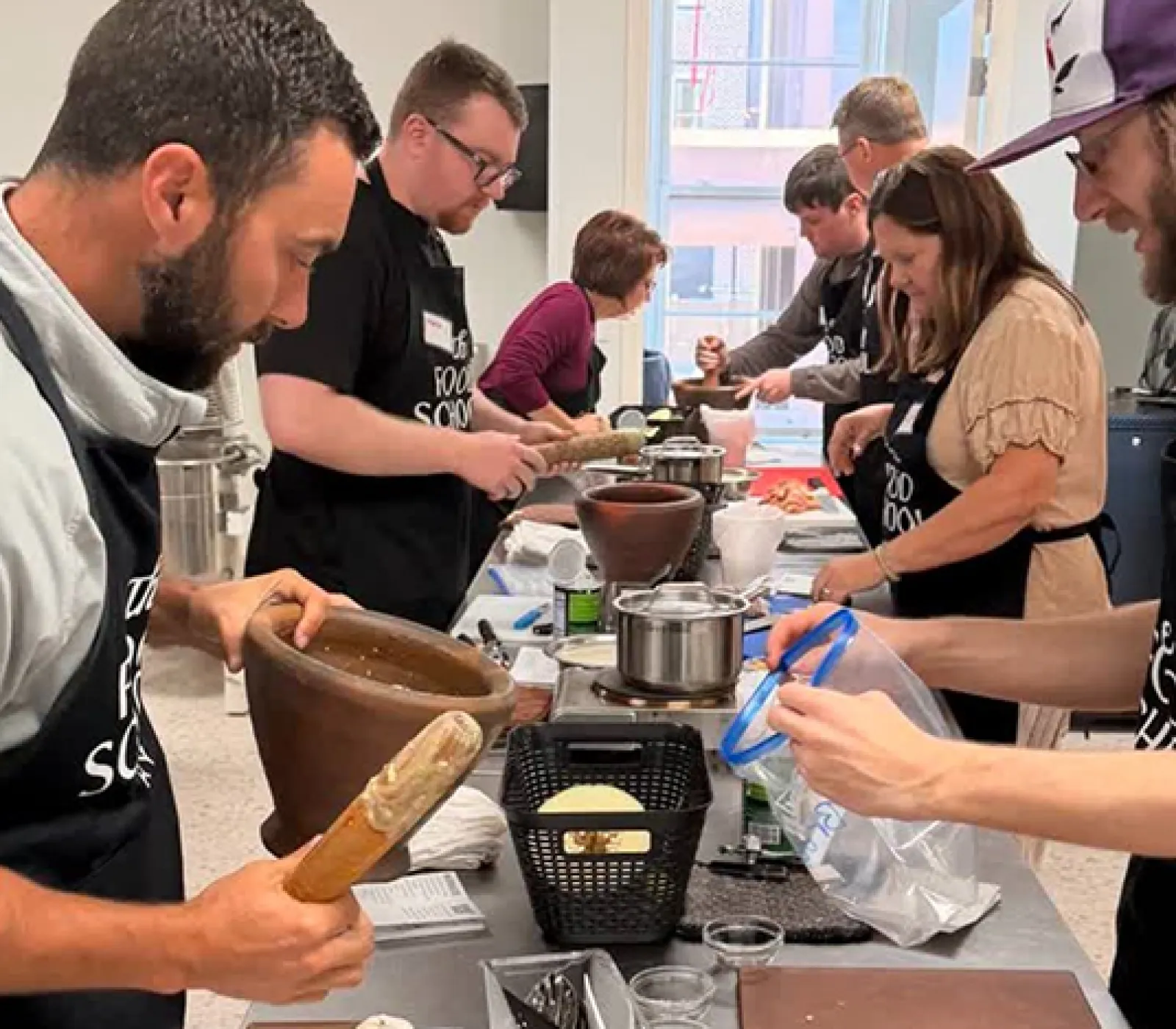 LifeWorks participants at seen preparing food down a long counter working with staff members to prepare food.