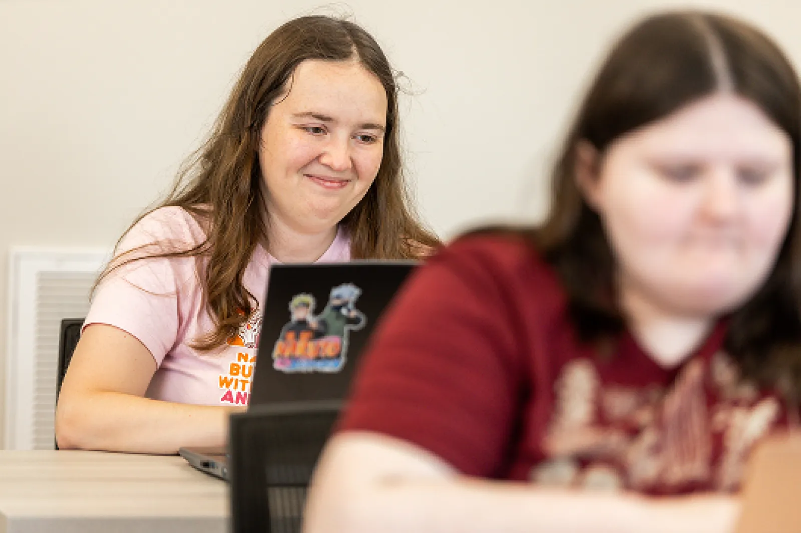 A female LifeWorks participant is working on her laptop and smiling in a classroom.
