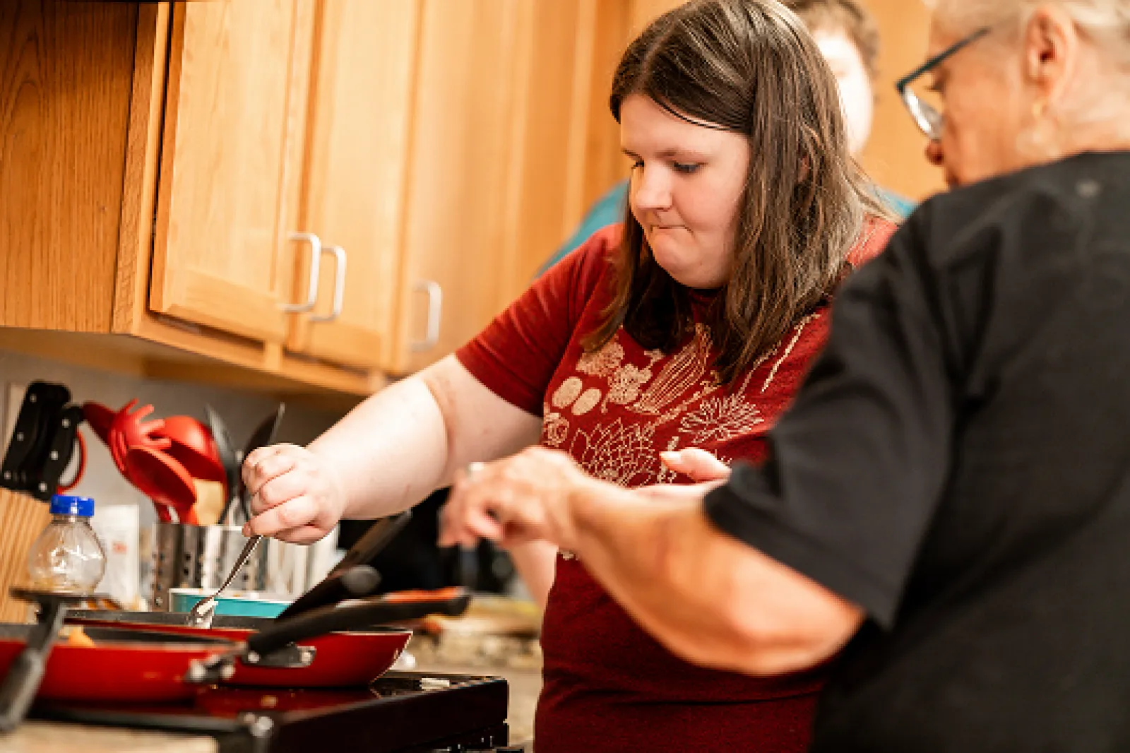 A female LifeWorks instructor is working with a female participant preparing food in a red skillet on a stove.