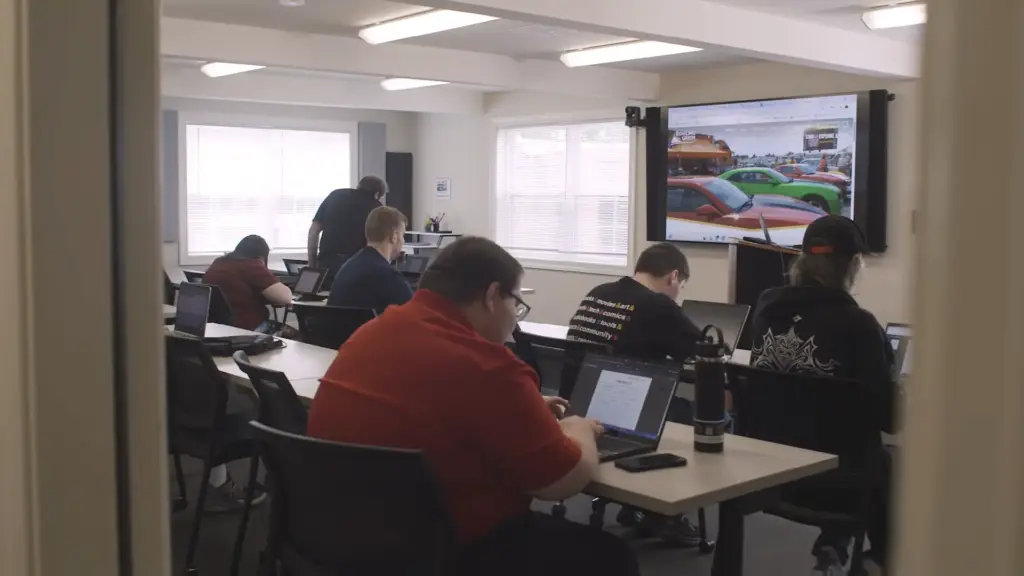 LifeWorks classroom photo with five participants working on laptops and a staff member helping one of them with the Bowling Green website on a projector screen